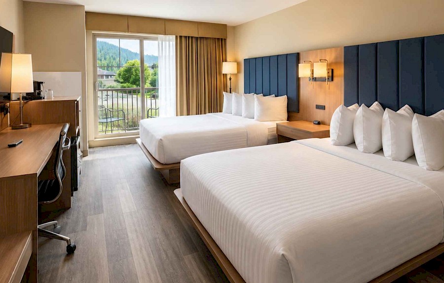 Modern hotel room with two queen beds, dark blue headboards, and a private balcony at St. Eugene Resort