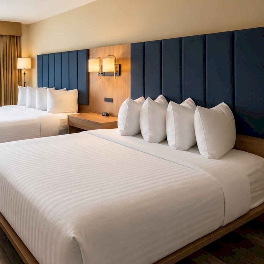Modern hotel room with two queen beds, dark blue headboards, and a private balcony overlooking trees.