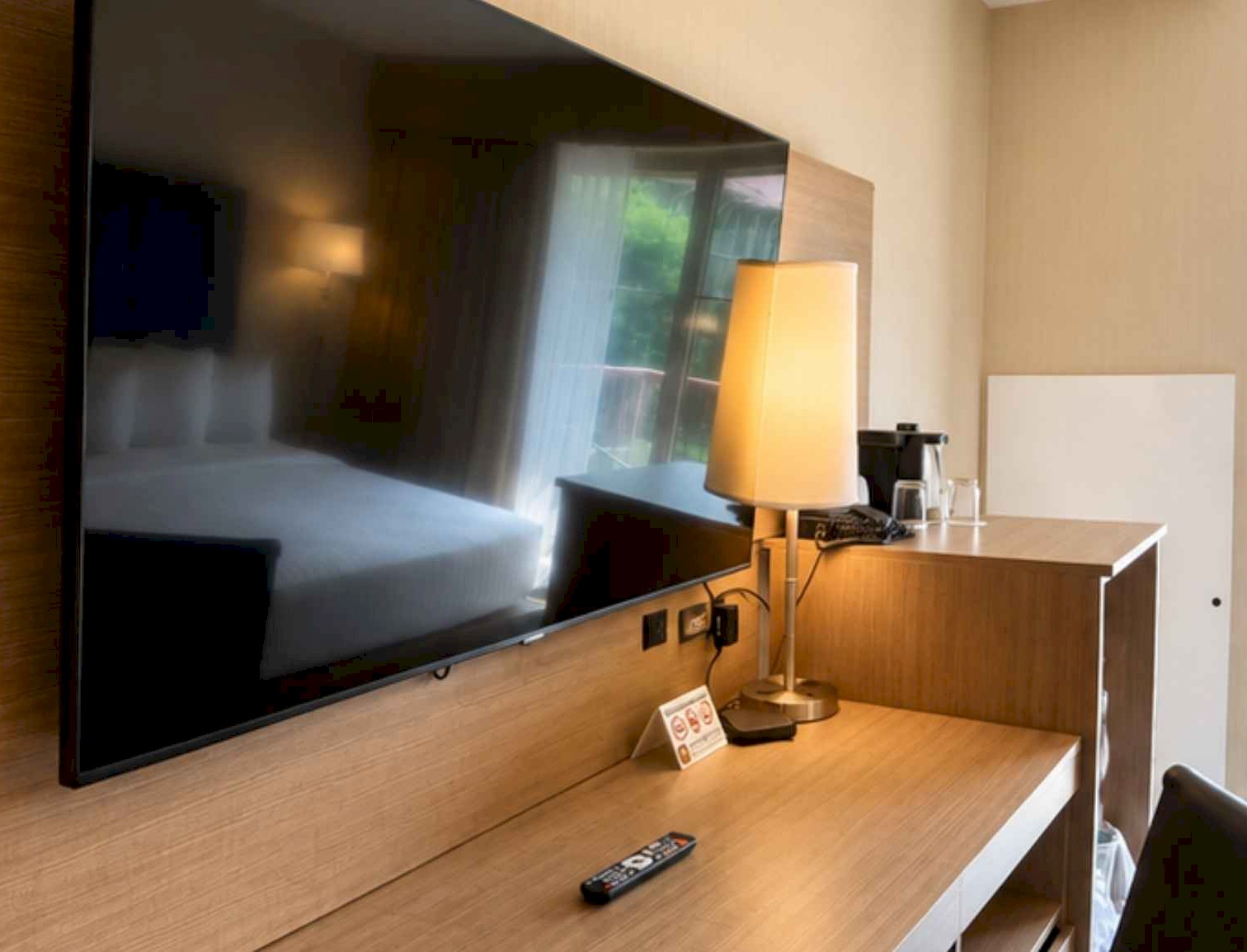 Flat screen TV mounted above a wooden desk in a brightly lit hotel room.