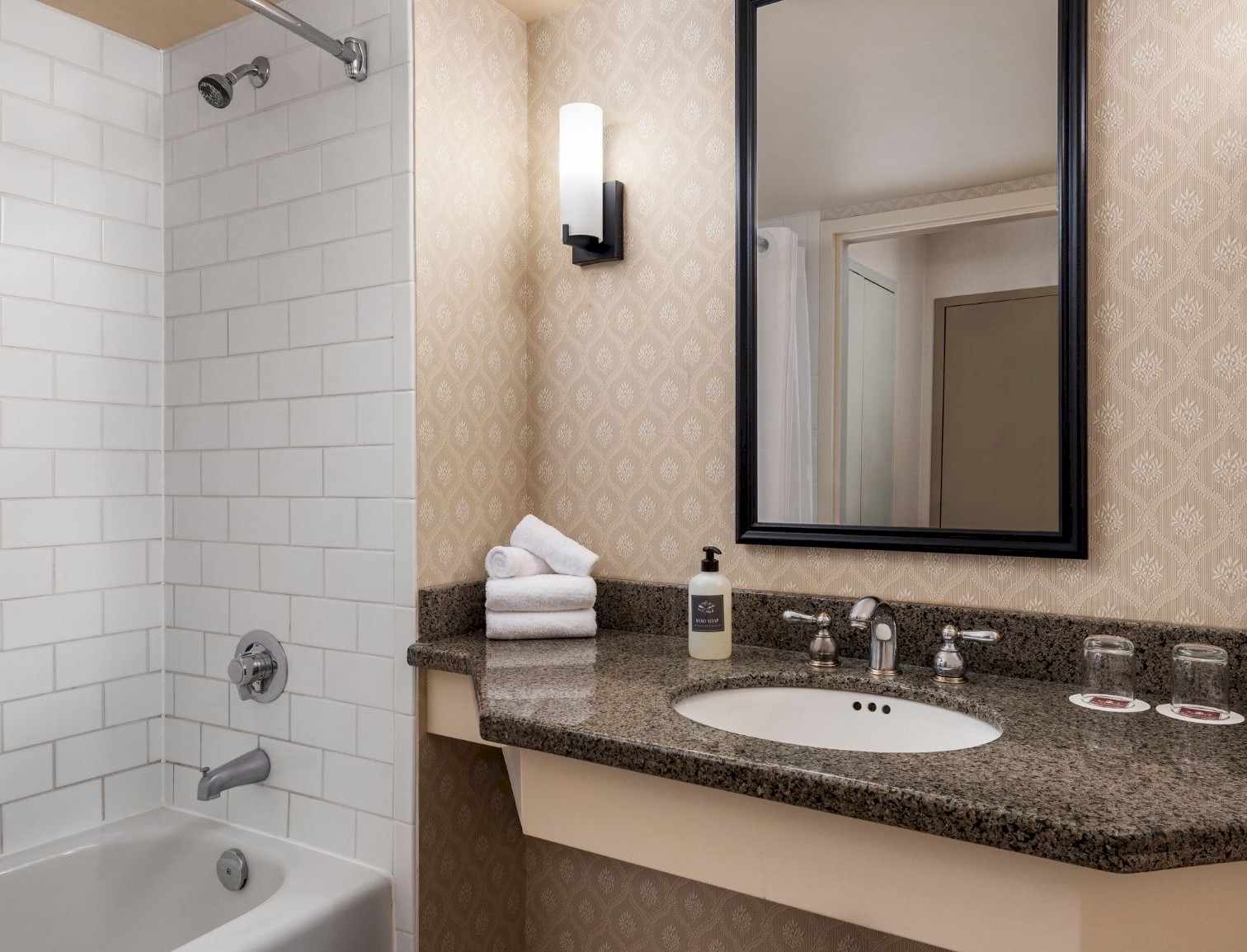 Hotel bathroom featuring a granite vanity, black-framed mirror, and a white subway-tiled bathtub shower.